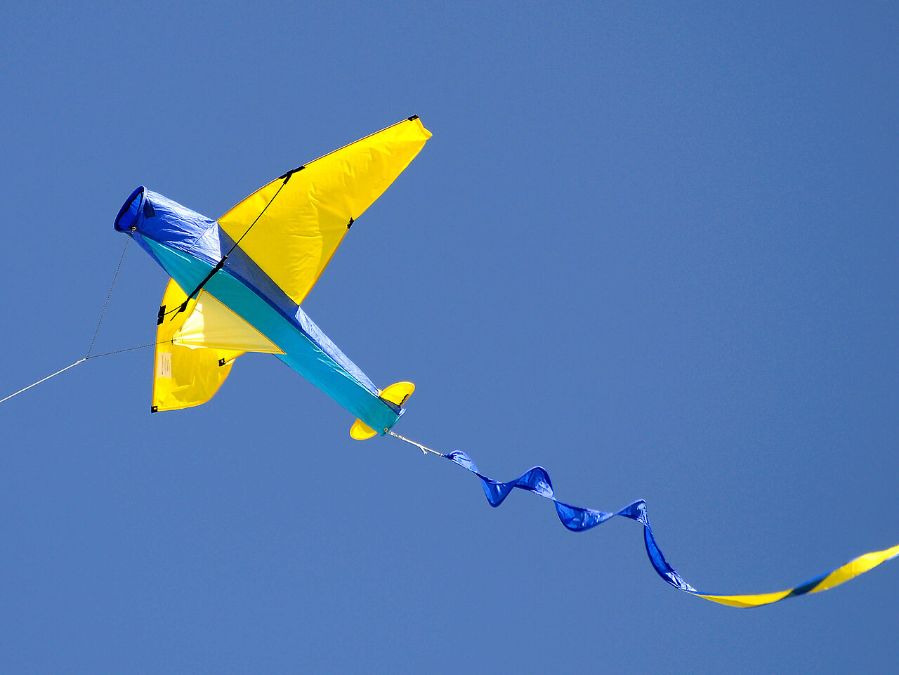 Das Bild zeigt einen gelb-blauen Lenkdrachen am wolkenlosen Himmel