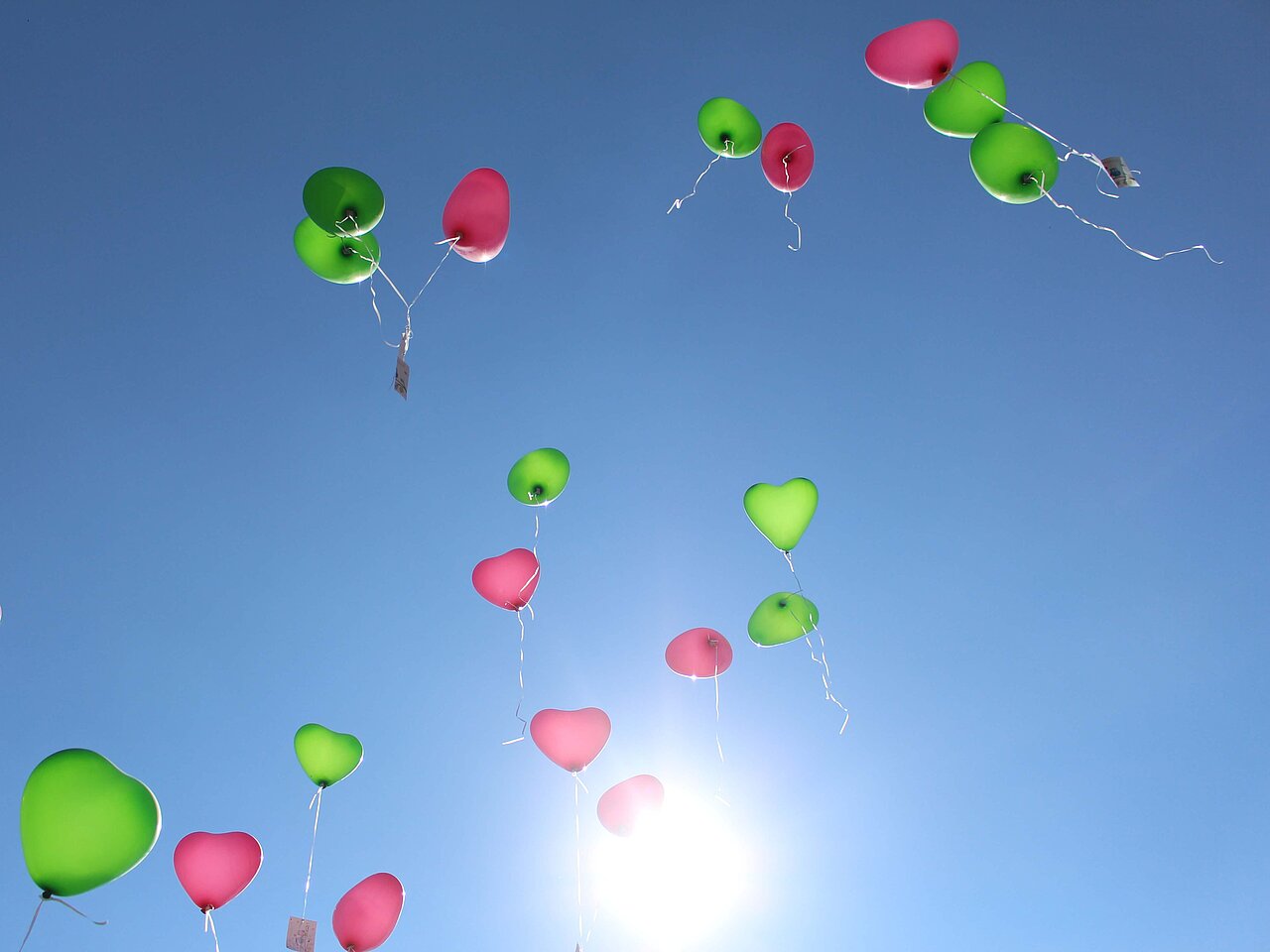 Das Bild zeigt wie gerade grüne und rote Luftballons in den Himmel aufsteigen